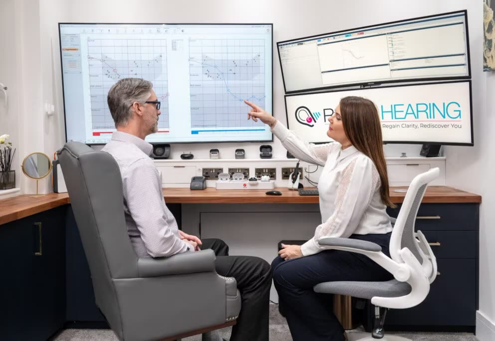 An audiologist at Regain Hearing pointing to an audiogram on a wall-mounted screen while a patient looks on.